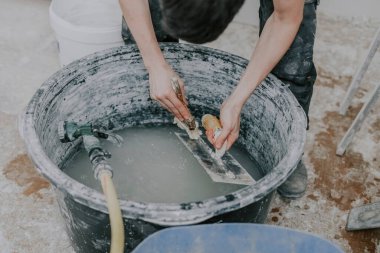 Siyah üniformalı genç beyaz bir adamın elleri, bir açıda duran, işi bitirdikten sonra, yakın çekimde, büyük siyah bir leğende bir fırça ve suyla spatula yıkar. İnşaat konsepti.