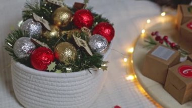 Bir sepette güzel noel dekoru ve kraft takvimini yuvarlak bir ahşap tepside yatak odasındaki yatakta yanan bir çelenkle ağır çekimde yakın çekim ve sağa doğru iz sürme şeklinde kutular..