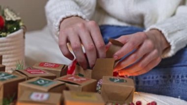 Beyaz örgü süveterli beyaz bir genç kızın elleri, yeni gelen takvim kutusundan ahşap çizme hediyesini çıkarır, bir odada bir yatakta oturur, alttan yavaş çekimde yakın çekim görüntüsü alır..