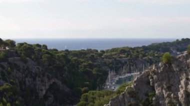Akdeniz ile kayalık dağların güzel panoramik manzarası Fransa 'nın güneyinde tekne ve teknelerle liman, yan manzara, yavaş çekimde yakın çekim ve uzaklaşma.