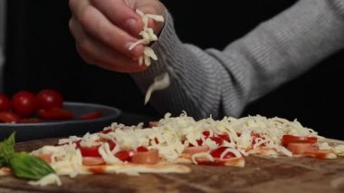 Kafkasyalı ergen kız, hamur hamuruna noel ağacı şeklinde mozzarella peyniri serpiştirir. Koyu çimento masasında malzemelerle dururlar. Yan görüntüyü yavaş çekerler. Bayram pizzası pişirme kavramını adım adım kavrayın..