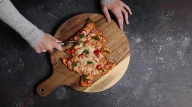 Beyaz kız ay bıçağıyla kesiyor ev yapımı pizza ağacı koyu çimento masasında duruyor, üst tarafı yavaş çekimde. Bayram pizzası pişirme kavramı, adım adım..