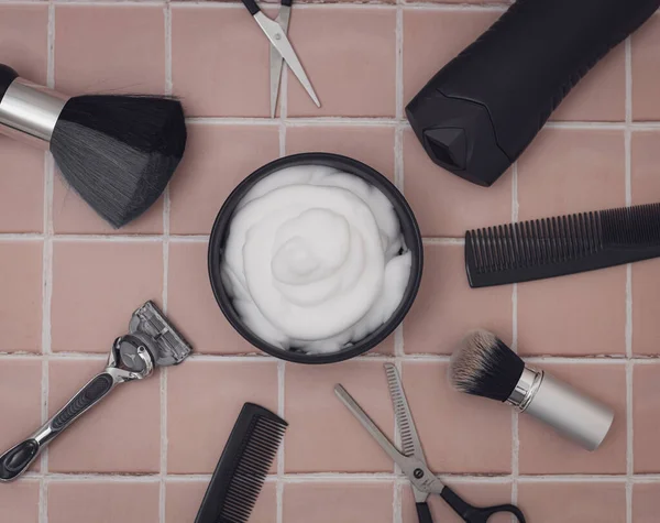 Shaving foam in a bowl, and around it are shaving brushes, a razor, aftershave cream, scissors, combs, thinning scissors on a flat lay brick tiled background close-up. The concept of a male hairdresser, beauty salon, beard shaving.