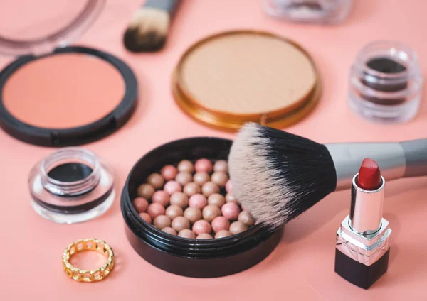 Granular face powder box with a makeup brush, jars of soft eyebrow shadows and hard texture powder boxes on a pink background, close-up side view with depth of field. The concept of cosmetics, beauty salon.