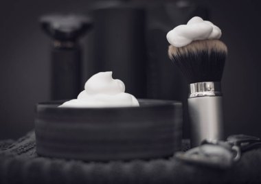 Tıraş köpüklü tıraş köpüğüyle tıraş köpüğü. Üzerinde bulanık tıraş kremi şişeleri, tıraş fırçası, elektrikli tıraş makinesi ve siyah arka planda jilet var. Yakın plan. Erkek kuaför konsepti, güzellik salonu, sakal sha