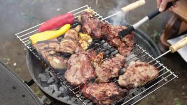 Genç, beyaz bir adam, evinin arka bahçesinde zoom ile yavaş çekimde dikilirken ızgarada maşayla kızartılmış sıcak, sulu bir bifteği ters çevirir..