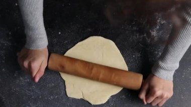 Kafkasyalı genç kız, koyu çimento masada dururken yuvarlak pizza hamuru ve oklavayla yuvarlıyor. Üst tarafı yavaş çekimde. Bayram pizzası pişirme kavramı, adım adım..