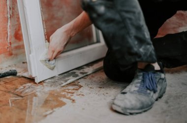 Kafkasyalı genç bir adam pencereyi sünger ve sabunla yıkarken eski fayanslı bir zeminde tek dizinin üzerinde duruyor, seçici bir odak ile yakın plan yan bakış. Ev yenileme konsepti, pencere çerçeveleri.