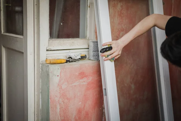 A caucasian young male with a bandaged injured finger with black scotch tape sweeps a window frame with a sponge with soapy water, close-up side view with selective focus. The concept of home renovation, washing window frames.