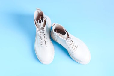 Açık mavi arka planda sert tabanlı eko-deriden yapılmış beyaz yarı sezonluk kestane rengi botlar, düz bir yakın plan. Kadın ayakkabısı konsepti.