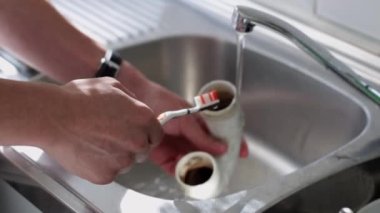 Kafkasyalı genç bir tesisatçının elleri kirli bir hortumu temizliyor ve duruluyor. Diş fırçasıyla lavaboda akan bir su akıntısının altında. Yan taraftan yavaş çekimde..