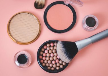 Granular face powder box with makeup brush, jars of soft eyebrow shadows and hard texture powder boxes on a pink background, flat lay close-up with selective focus. The concept of cosmetics, beauty salon.