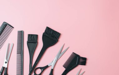 A set of hairdresser's tools from scissors,brushes and combs on a pink background with little copy space,flat lay close up. The concept of hairdressing, beauty salon, tools.