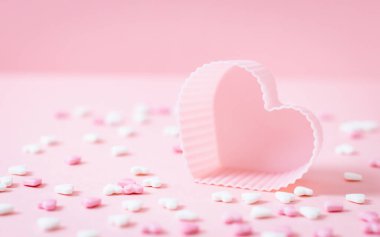 One muffin tin with scattered heart candy sprinkles lie on a pink background, close-up side view.Valentine's day concept.