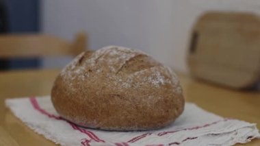 One round fresh rye bread with fiber on a white kitchen napkin lies on a wooden table in the kitchen with a zoom out, close-up side view.The concept of baking bread.