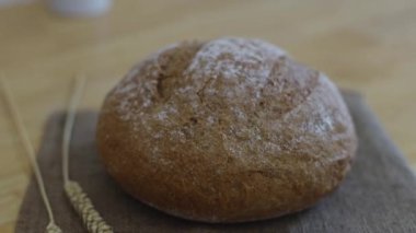 One round fresh rye bread with fiber on a baggy napkin with two ears lies on a wooden table in the kitchen with zoom out back, close-up side view.Bread baking concept.