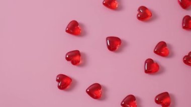 Lots of small red glass hearts lying on a pink background with tacking to the right, close-up top view. Concept of love, valentine's day.