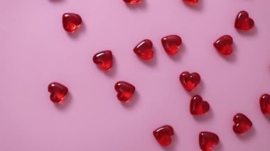 Many small red glass hearts lying on a pink background with a circular motion to the left, top view close-up. Concept of love, valentine's day.