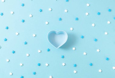One empty heart cupcake pan and star candy sprinkles lie on a blue background, closeup flat lay. The concept of Valentine's Day, the birth of a son, wedding, gender party.