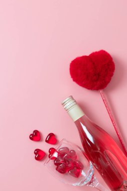 One bottle of wine, a glass with glass hearts pouring out of it and a pen lie on a pink background, flat lay close-up. The concept of love and the holiday of Valentine's Day,wedding.
