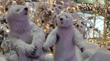 Beautiful polar bears standing at the New Year's exhibition under the Christmas tree exhibition in the store moves its head, side view, close-up. Concept of moving toys, holiday exhibition.