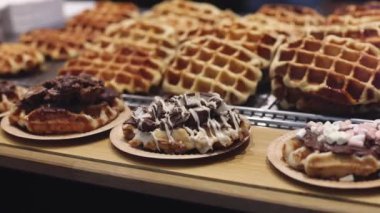 Appetizing Belgian waffles with chocolate and caramel filling with cream in craft disposable plates lie on the counter in the store, close-up side view with a smooth circular zoom. Waffle shopping concept.