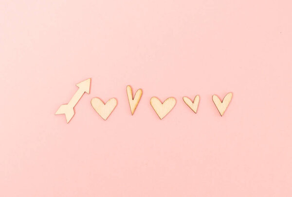 Five wooden hearts and one arrow lie in a row in the center on a pink background, flat lay close-up. The concept of wooden decorations, valentine's day, love day.