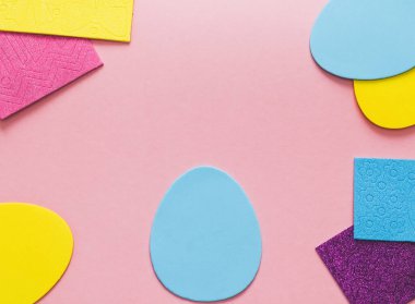 Colored felt set of eggs and patterned stickers framed on the sides on a pink background with copy space in the center, flat lay close-up.Concept diy, crafts, children art, at home, artisanal, needlework, easter.