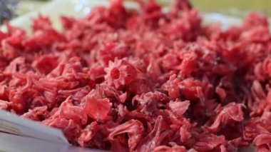 Appetizing dried fruit red hibiscus flower in a white tray lie on the counter in the store, side view close-up with a smooth circular zoom. Candied fruits shopping concept.