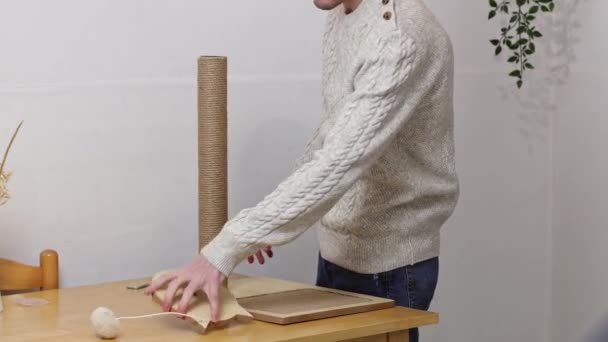 Young Caucasian Man Knitted Sweater Assembles Creative Wooden Scratching Post — Stock Video