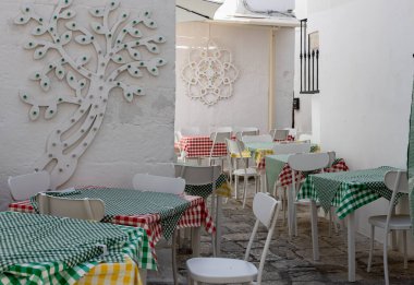 Beautiful view of the tables with checkered tablecloths of a home restaurant with carved decoration on white walls in the city of Ostuni Italy, close-up side view. Ancient architecture concept.