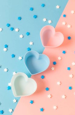Three heart cupcake pans and star candy sprinkles lie in the center on a pink and blue background, close-up flat lay. Valentine's day concept, gender party, wedding.