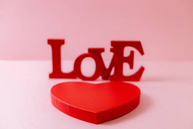 Red cardboard box and wooden solid word Love lie in the center on a pink blurred background, close-up side view. Valentine's day concept.