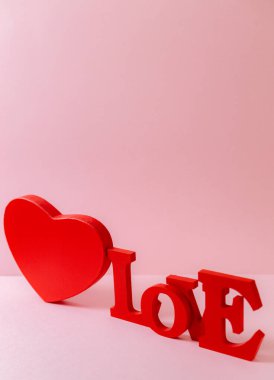 A red cardboard box and a wooden whole word Love lie diagonally to the right on a pink background, close-up side view. The concept of Valentine's day, love day.