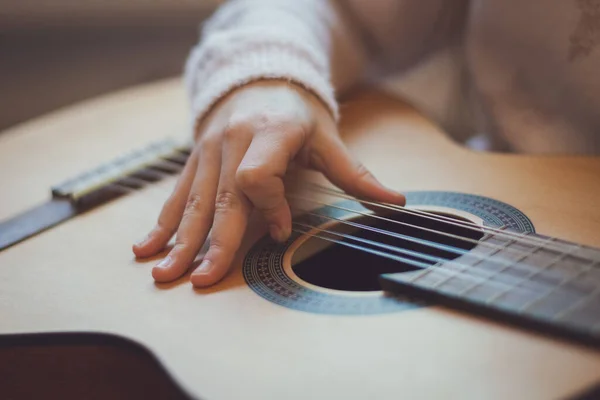 A little caucasian girl holds a guitar on her knees and plucks the strings with her fingers, close-up side view. Music education concept.