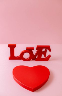 Red cardboard box and wooden solid word Love lie diagonally on a pink background, close-up top view. Valentine's day concept.