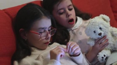 İki güzel beyaz esmer kız, yatmadan önce birlikte çizgi film izliyorlar. Akşamları turuncu bir kanepede oturuyorlar. Çizgi film izleme kavramı..