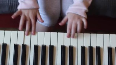Hands of a little caucasian unrecognizable girl playing the electric piano, plucking the keys with her fingers, sitting on the sofa in the room, top view close-up. Music education concept.