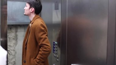 A young handsome caucasian brunette man in a brown coat rises in an elevator up and stops going to the floor,side view close-up.Men lifestyle concept.