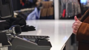 One young caucasian unrecognizable man in a brown coat takes out a black wallet from his pocket to pay for purchases in a store, close-up side view. Offline shopping concept, modern lifestyle.