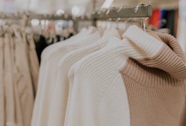 White knitted turtleneck sweaters and brown cardigans hang on hangers on a stand in a clothing store, close-up side view with selective focus.Offline shopping concept.