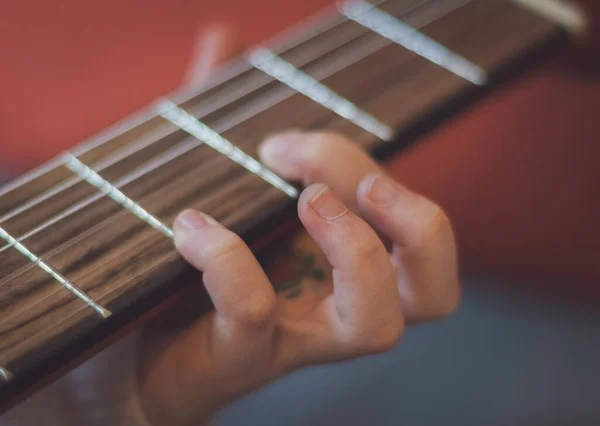 Little caucasian girl holding a guitar and pinching the strings with her fingers, close-up side view. Music education concept.