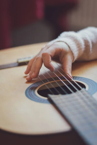 A little caucasian girl holds a guitar on her knees and plucks the strings with her fingers, close-up side view. Music education concept.