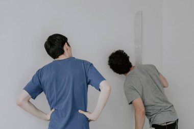 Two young beautiful Caucasian plasterers in work clothes and with brown hair hold large spatulas in their hands and check the evenness of the wall after puttying in the room, close-up side view. The