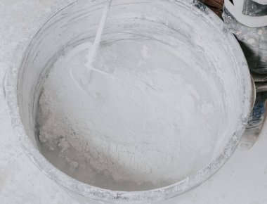 A large black basin with dry putty, water and an electric mixer inside lie on the floor in an apartment where repairs are underway, and a worker stands nearby, close-up view from above. The concept of