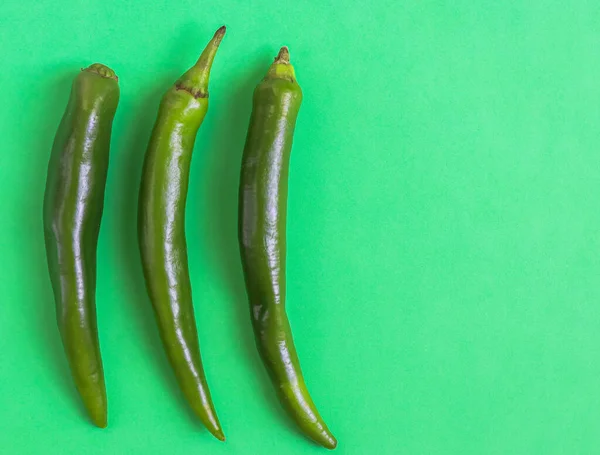 Three hot green chili peppers lie on the left on a green background with copy space on the right, flat lay close-up. The concept of Cinco de Mayo, minimalism, blanks.