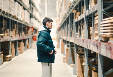 One young handsome caucasian brunette guy standing sideways carefully looks at the product on the shelf in the store, side view close-up. Concept of offline shopping.