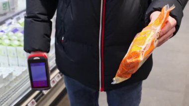 Genç bir adam bir mağazada dikilirken plastik bir torba dolusu taze makarna ile barkodu tarıyor. Çevrimdışı alışveriş konsepti..