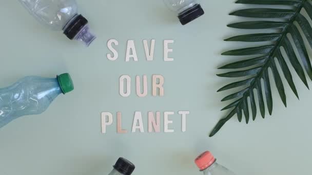 ボトルからのプラスチックごみ ヤシの木の枝 木製の文字の碑文 私たちの惑星を保存ライトグリーンの背景に フラットレイアップに横たわっている 生態系と環境汚染の概念 — ストック動画