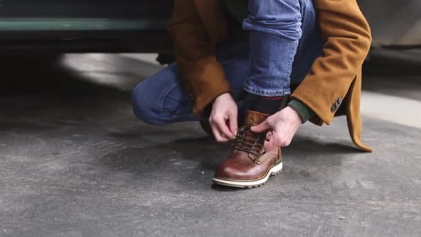 Молодой Кавказский Мужчина Коричневом Пальто Зашнуровывает Новую Обувь Ногу Приседая — стоковое видео